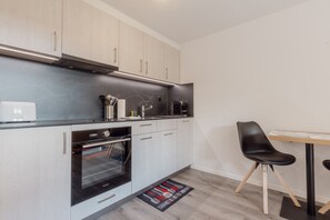 A modern kitchen with white cabinets, a built-in oven, and a black countertop. - Charmant Studio Rénové à Grimentz (Grimentz)