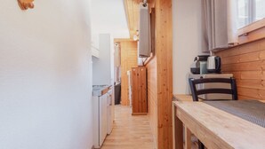Un estrecho pasillo con paredes de madera, una zona de cocina con electrodomésticos y una mesa de comedor con sillas.