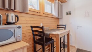 Cocina pequeña con microondas, hervidor y mesa de madera con sillas.