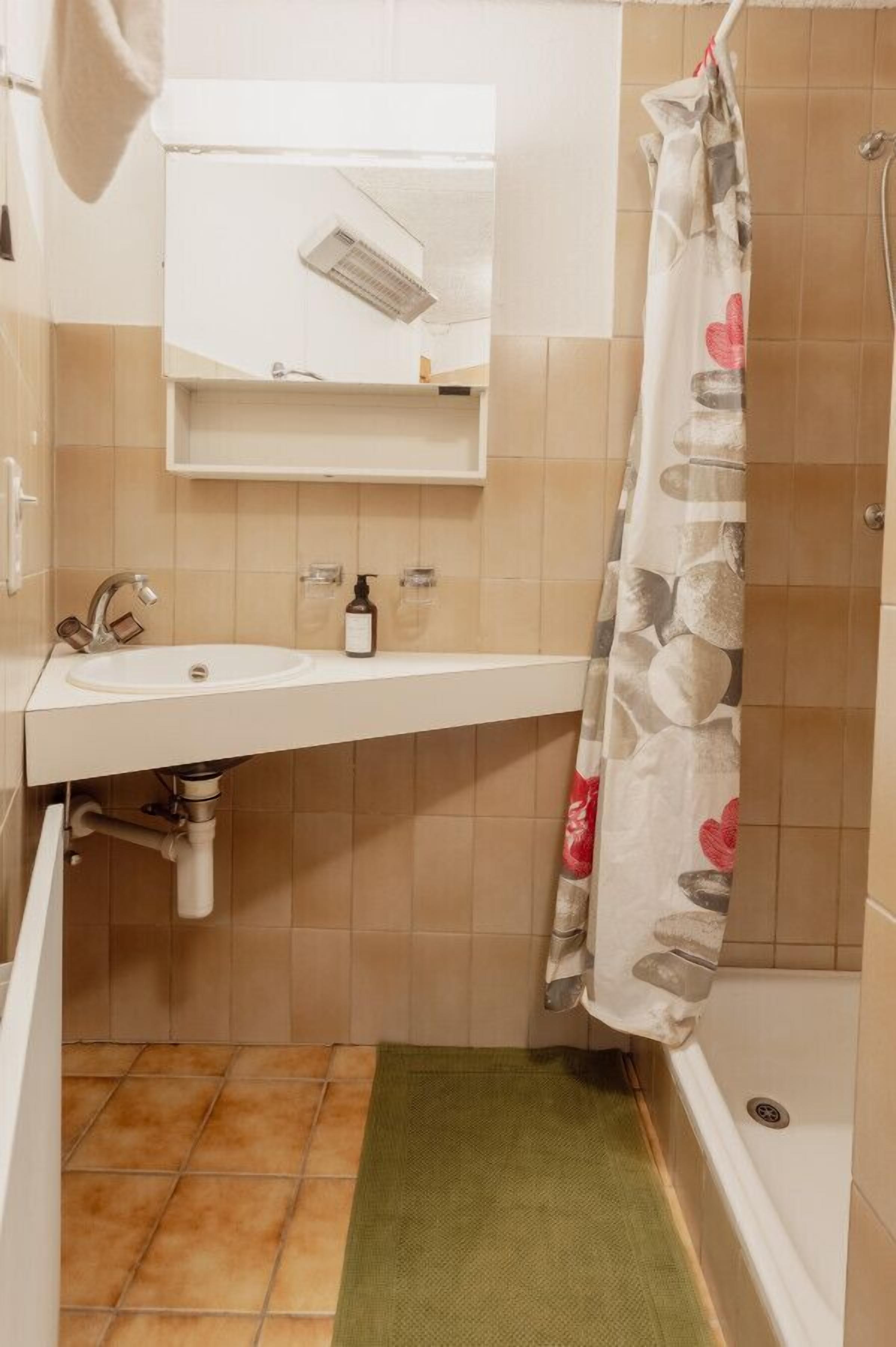 A bathroom with a white sink, a mirror above it, a shower curtain with a floral pattern, and a green bath mat.