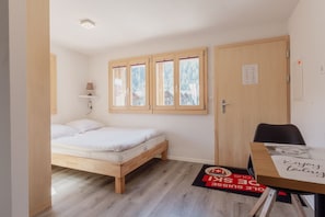 A small, well-lit room with a single bed, a desk, and a window with a view of trees.