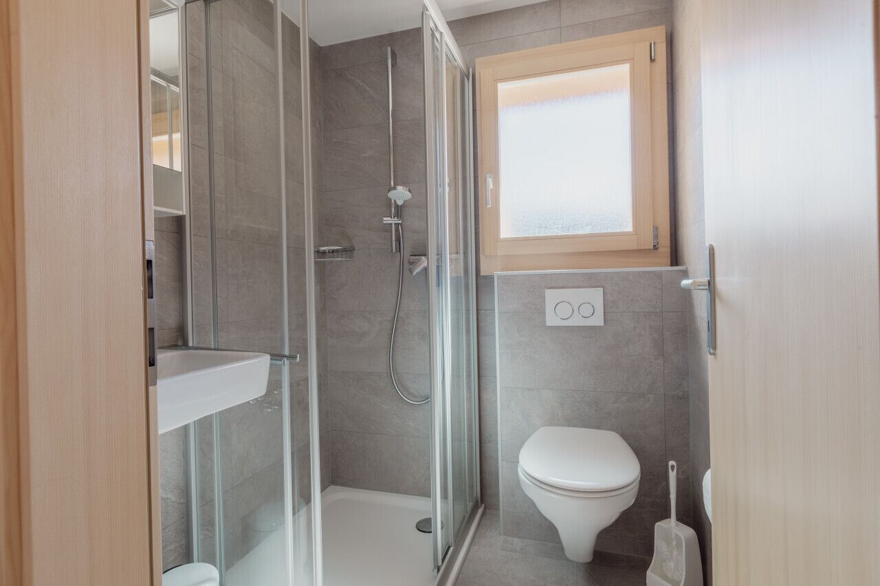 Une salle de bain moderne avec une douche à parois de verre, des toilettes et une fenêtre au-dessus du lavabo.