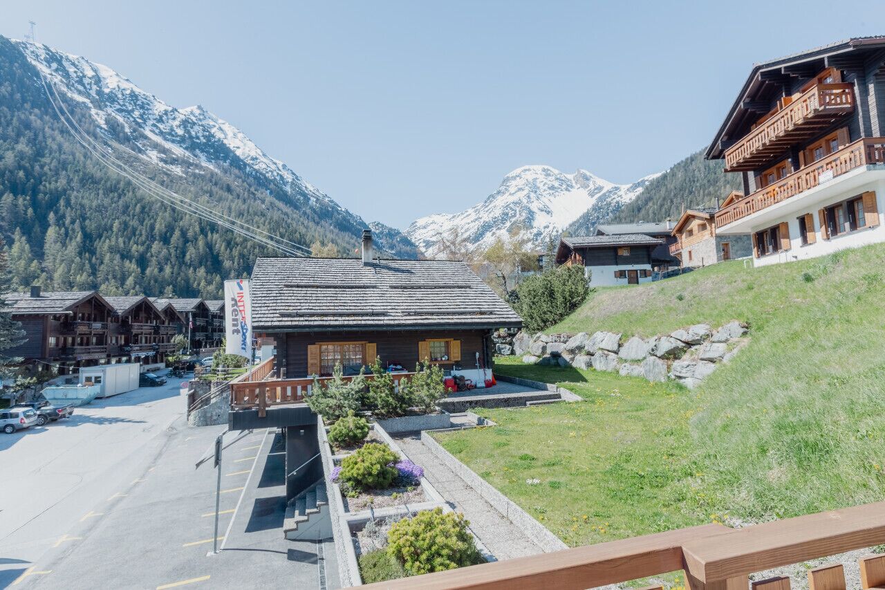 Un chalet de montagne avec une façade en bois, un espace de stationnement et une vue sur des montagnes enneigées.