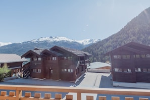 Ein Chalet-ähnliches Holzhaus mit Balkon, vor einer Kulisse schneebedeckter Berge.