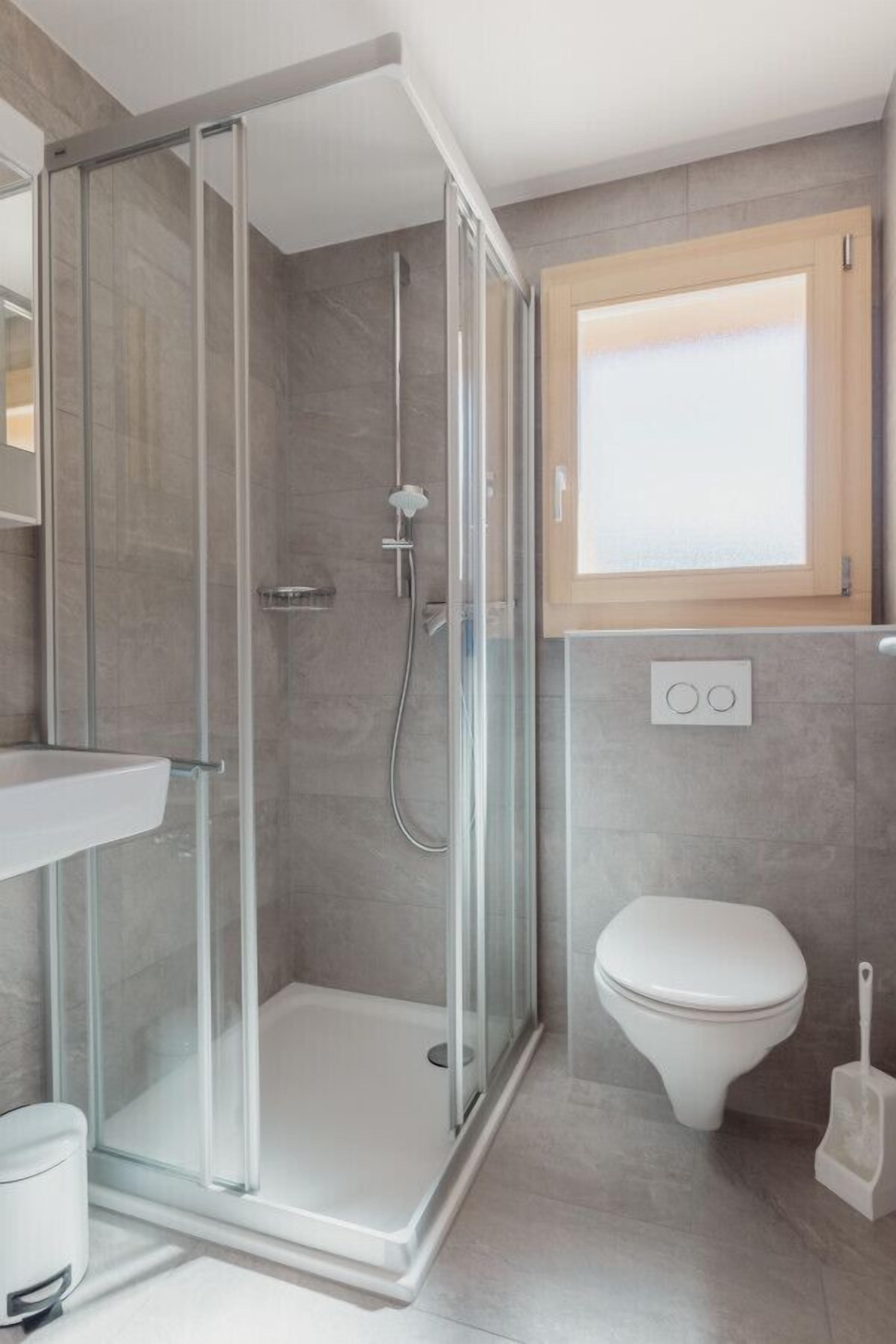 A modern bathroom with a glass-enclosed shower, a white toilet, and a visible light switch.