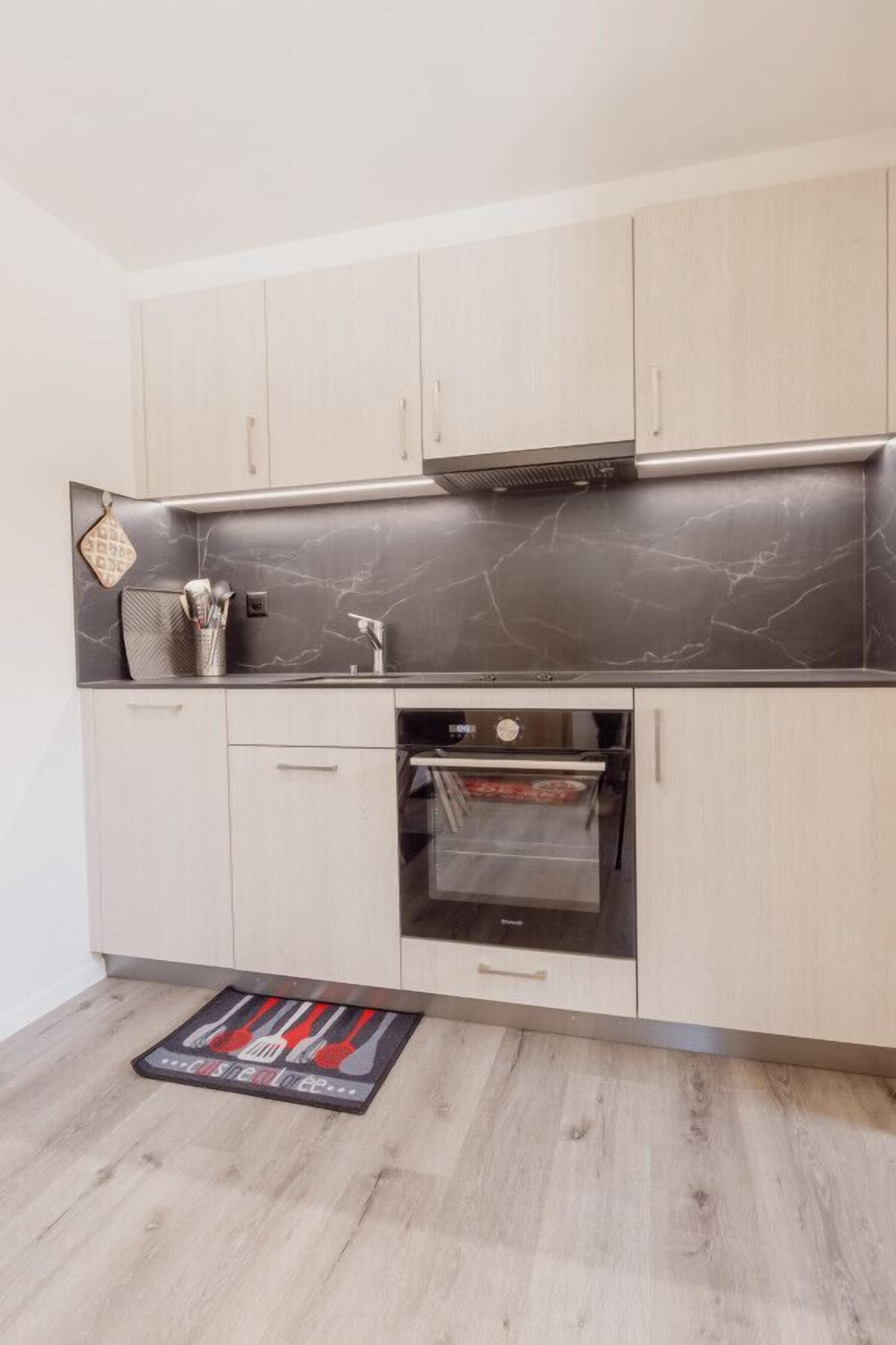 A modern kitchen with light wood cabinets, a dark marble backsplash, and a built-in oven.