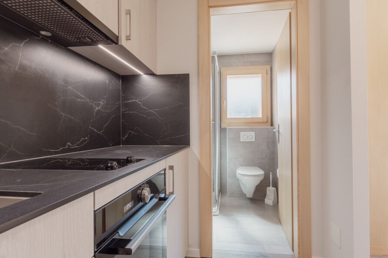A modern kitchen with a black marble backsplash, a stainless steel range hood, and a built-in oven.