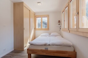 Une chambre avec un lit en bois, une armoire et une fenêtre donnant sur les montagnes.