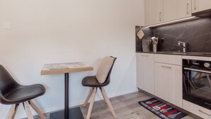 Una cocina compacta con zona de comedor, que incluye una mesa pequeña, dos sillas, encimera de mármol y horno empotrado.