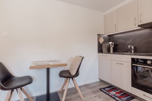 Eine kompakte Küche mit Essbereich, ausgestattet mit einem kleinen Tisch, zwei Stühlen, einer Marmorarbeitsplatte und einem Einbauofen.