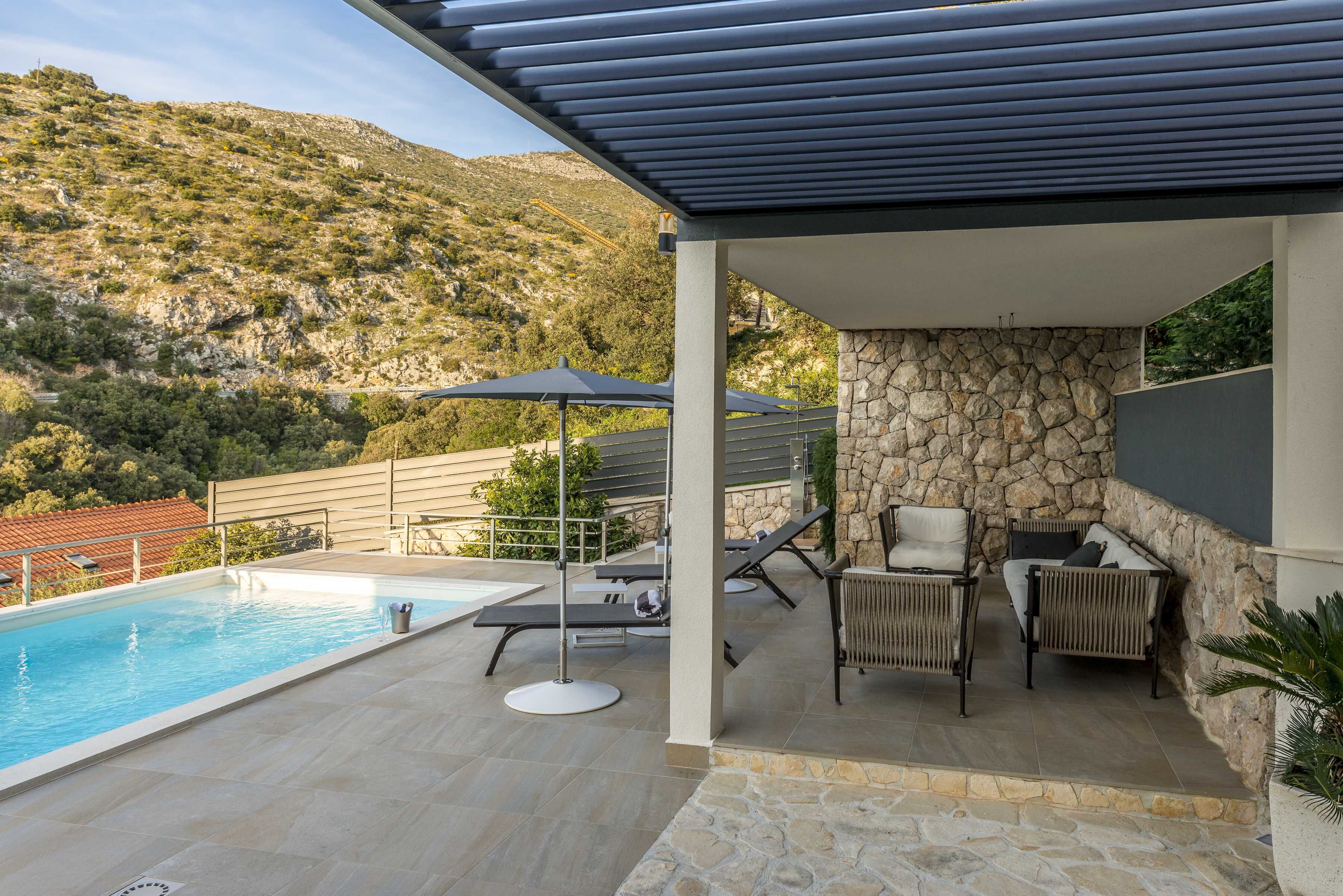 Zona de piscina con pared de piedra, sillas de descanso y sombrillas.
