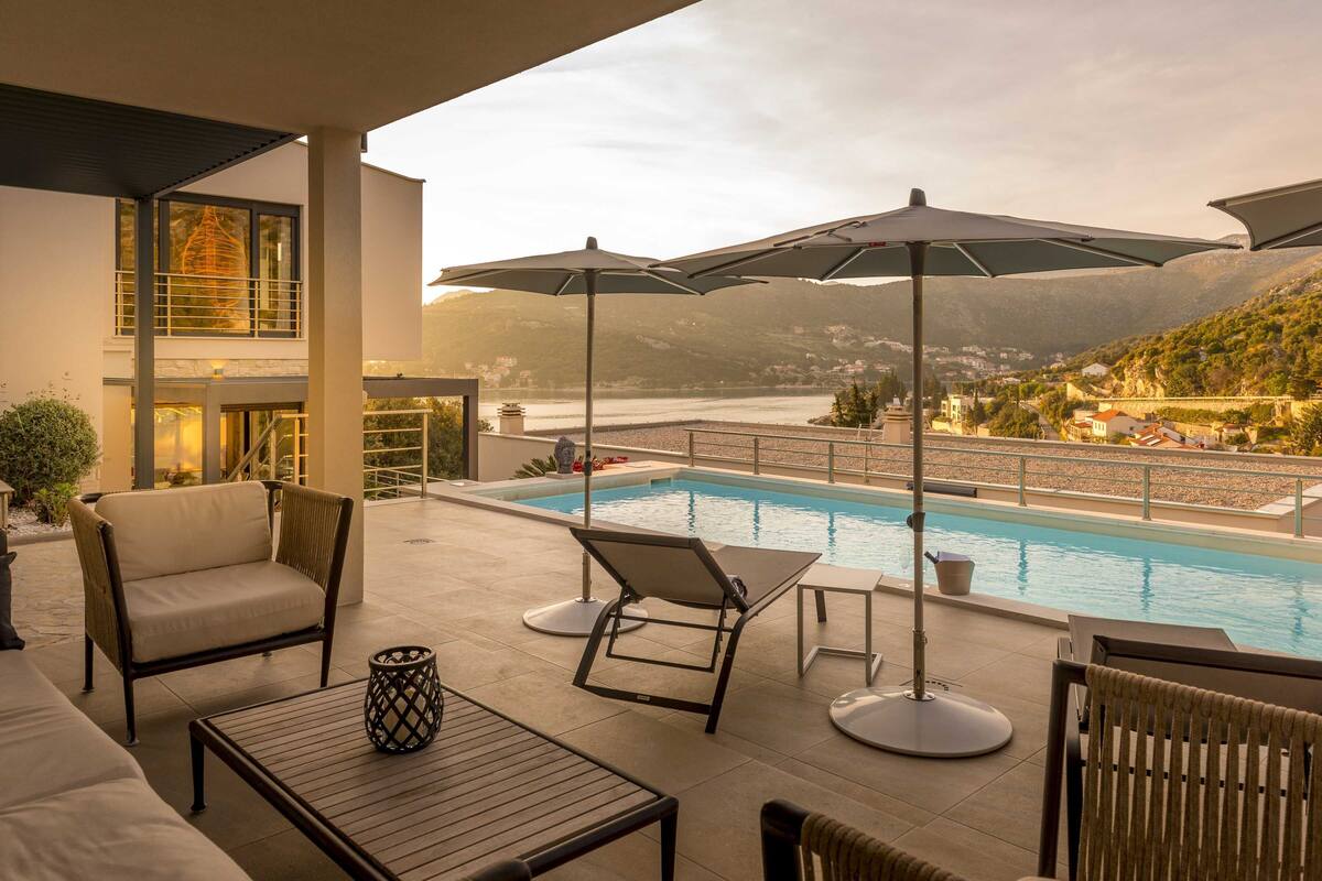 Zona junto a la piscina con sillones de descanso, sombrillas y vistas a un lago y montañas.