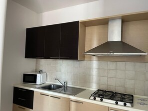 A modern kitchen with black cabinets, a stainless steel range hood, a microwave, a sink, and a gas stove.