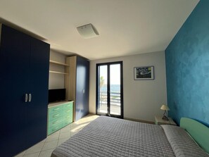 Une chambre à coucher avec un lit, une armoire, un bureau avec une chaise, un tableau au mur et une vue à travers une porte.