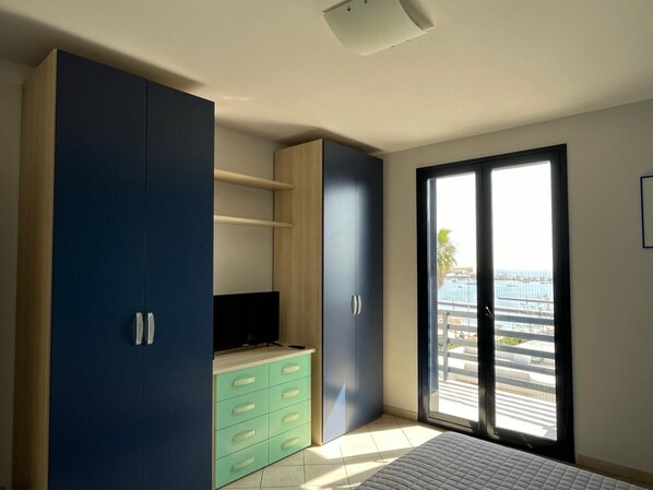 Une chambre à coucher avec un lit, un téléviseur posé sur un meuble, une armoire et une porte coulissante donnant sur un balcon.