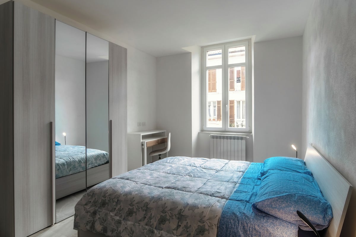 A bedroom with a bed, a wardrobe, a desk, and a window.