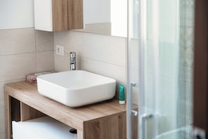 Un baño con lavamanos blanco, encimera de madera y puerta de cristal para la ducha.