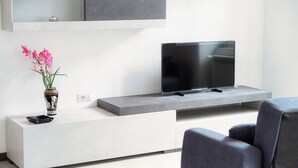 Moderni olohuone, jossa on seinään upotettu hylly, jonka päällä on litteänäyttöinen televisio, maljakko kukkineen ja harmaa sohva.