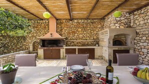 Eine Terrasse im Freien mit Steinmauern, einem Backofen aus Ziegeln und Sitzgelegenheiten.