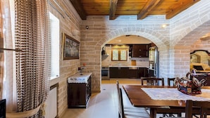 Ein rustikales Interieur mit freiliegenden Backsteinwänden, einer Holzbalkendecke, einer Essecke mit Tisch und Stühlen sowie einer durch einen Bogen sichtbaren Küche.