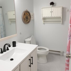 A bathroom with a white sink, black faucet, and a toilet. There is a mirror above the sink and a cabinet with a clock above the toilet. - Cozy 3 beds with Pool ,Balcony and walk to the beach (Ocean City)