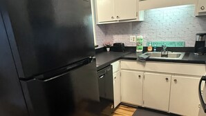 A kitchen with a black refrigerator, white cabinets, a wooden floor, and a coffee maker on the counter.