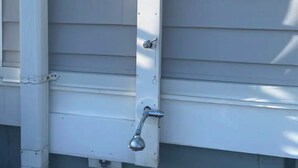 A white exterior wall with a vertical metal bracket and a green hose attached to it.