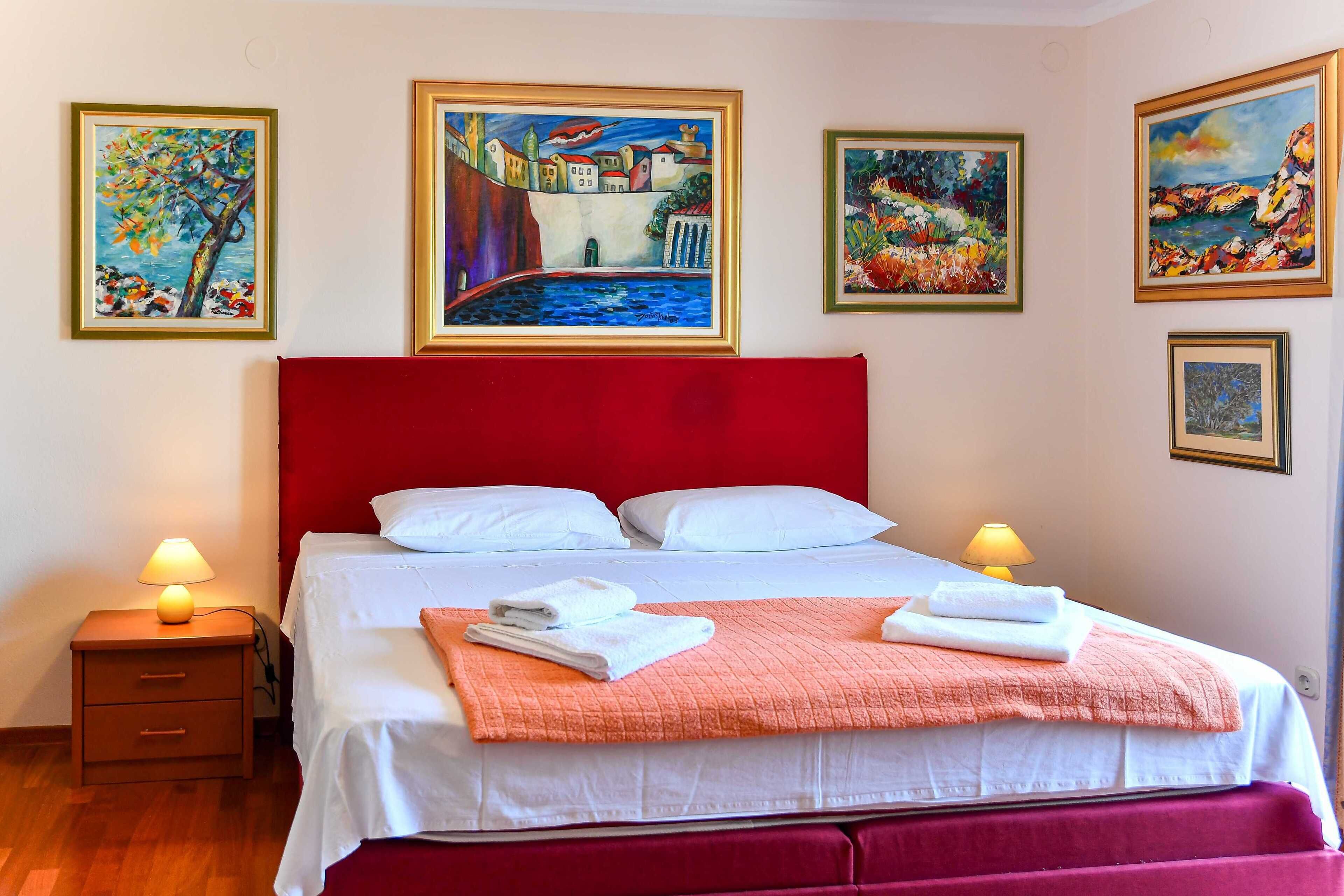 Una habitación de hotel con un cabecero rojo, ropa de cama blanca y varias pinturas en las paredes.