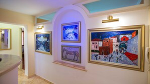 A hallway with framed artworks on the walls, a marble floor, and a light fixture above. - Holiday Home Lapad Beach Royal (Dubrovnik)