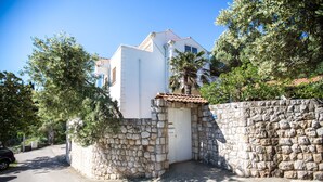A white building with a stone wall entrance, a palm tree, and a clear blue sky. - Holiday Home Lapad Beach Royal (Dubrovnik)