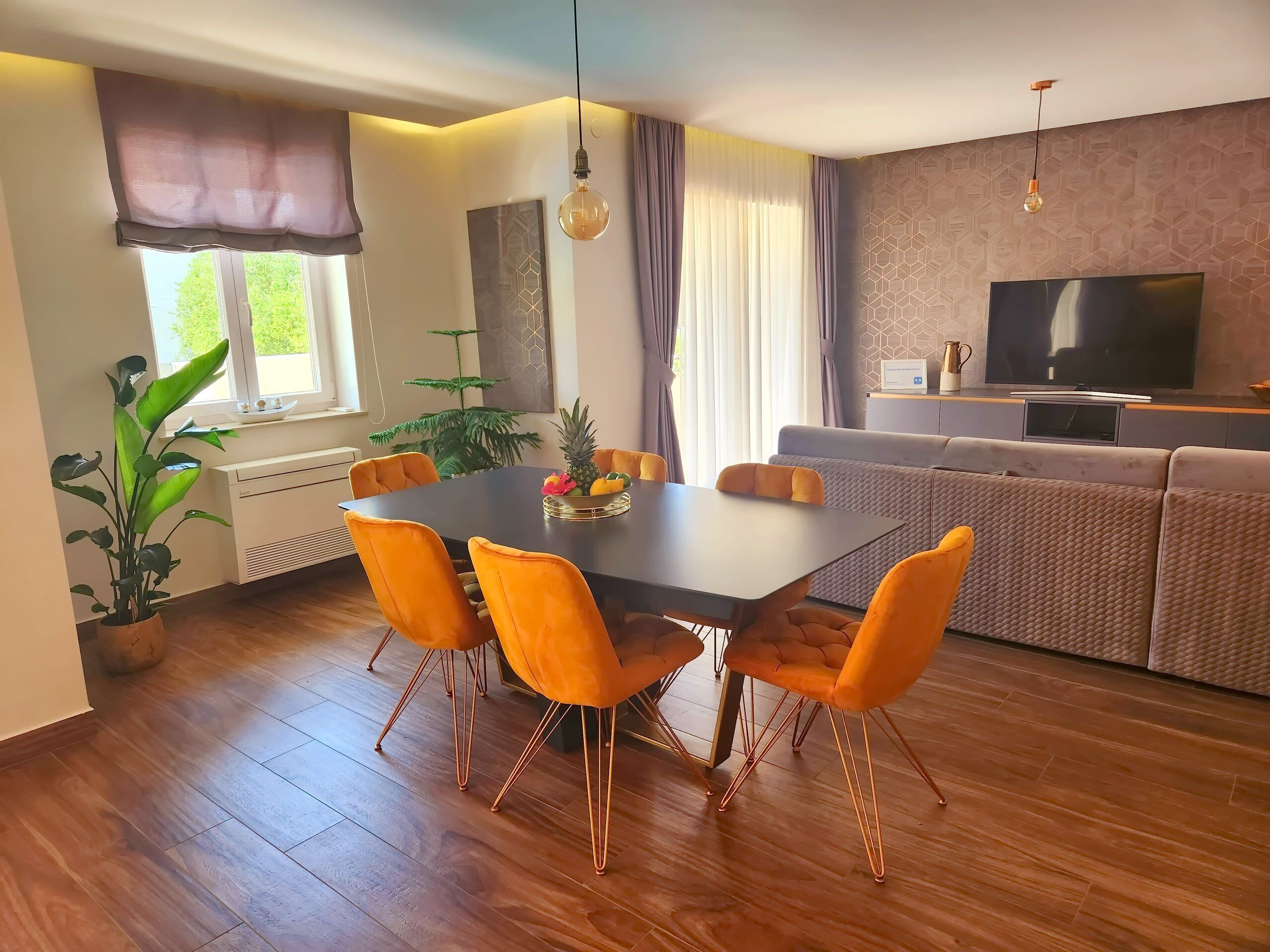 Una sala de estar moderna con comedor, que incluye un televisor grande, asientos cómodos y una planta en maceta.