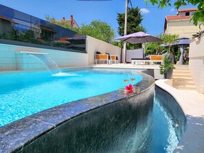 A swimming pool with a waterfall feature, surrounded by outdoor seating and potted plants. - Villa Calypso Royal Apartment (Zadar)