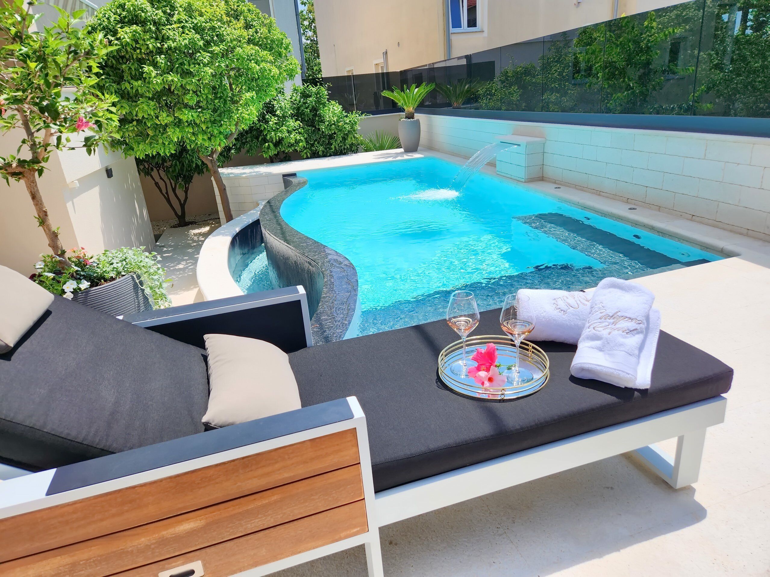 A poolside lounge with a curved pool, a glass barrier, and a white towel with a monogram.