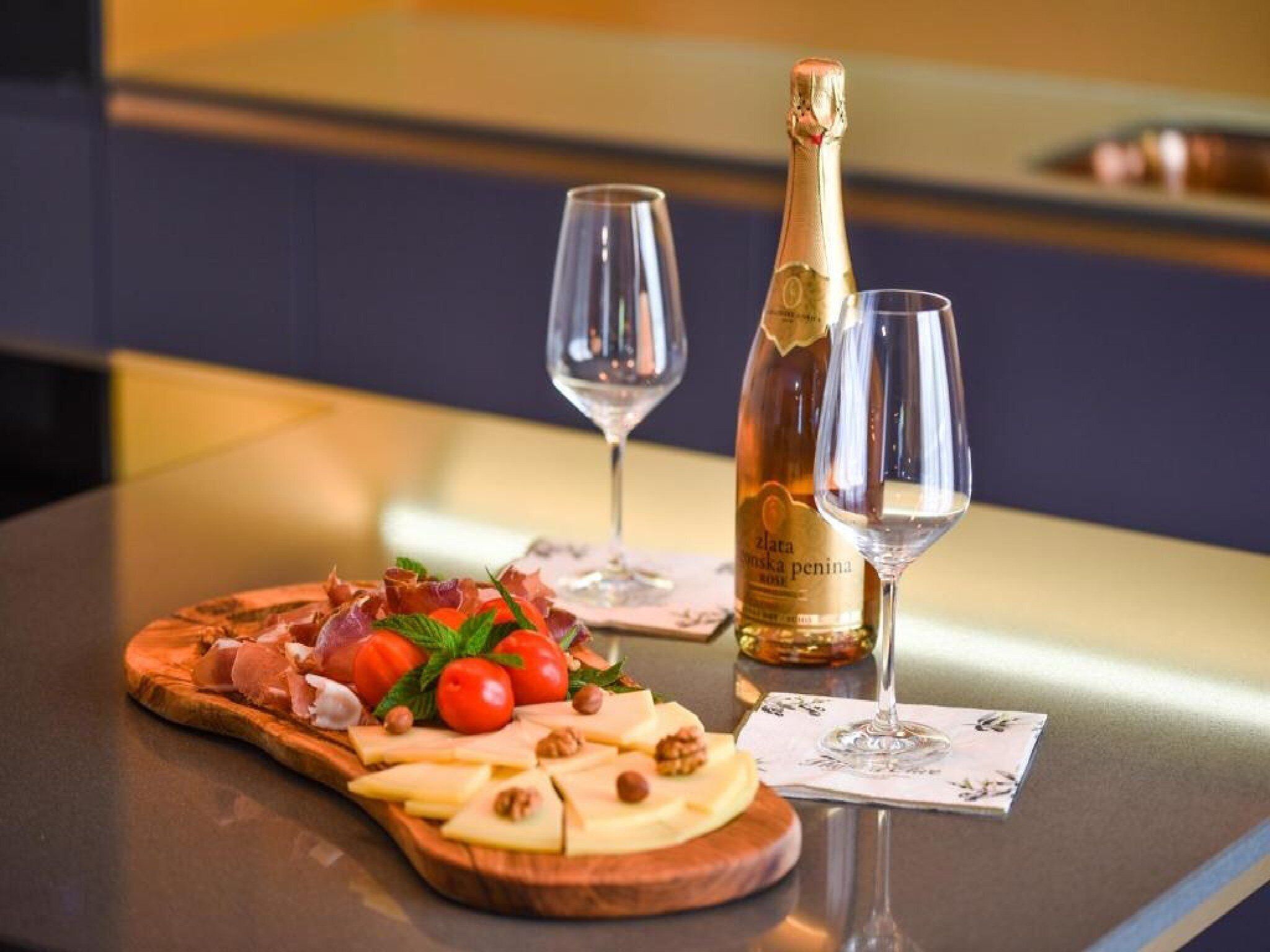 Ein Holzboden mit Käse, Tomaten, Nüssen, einer Champagnerflasche und zwei Gläsern auf einem Tisch.