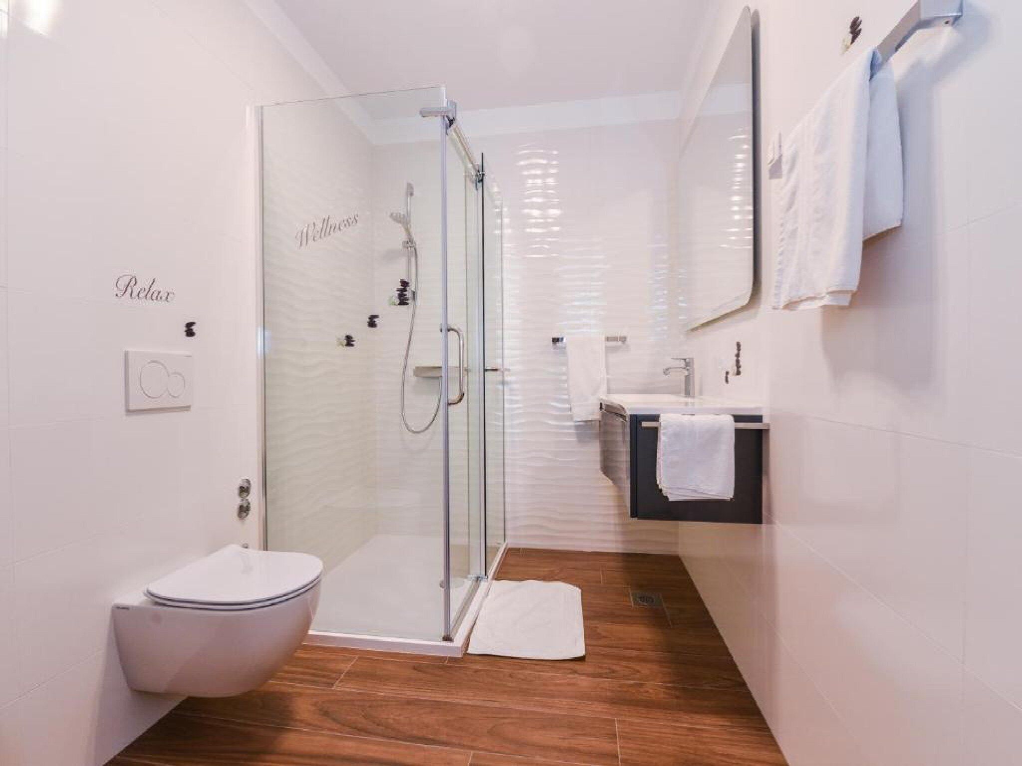 A modern bathroom with a glass shower enclosure, a toilet, a sink, and a mirror.