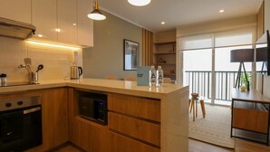 A modern kitchen with wooden cabinets, a built-in oven, and a coffee maker. There is a small island with a welcome sign and two bottles. The kitchen leads to a balcony with a view. - w * | Splendid 1BR in the Heart of Barranco (Lima)