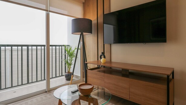 A modern living room with a glass table, a wooden cabinet, a floor lamp, and a TV mounted on the wall. - w * | Splendid 1BR in the Heart of Barranco (Lima)