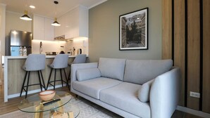 A modern living room with a light grey sofa, two grey chairs, a glass coffee table, and a kitchen in the background. - w * | Splendid 1BR in the Heart of Barranco (Lima)