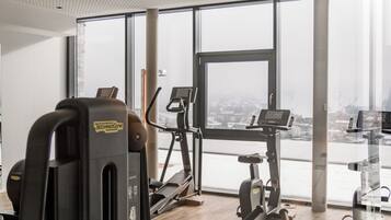 A gym with various exercise machines, large windows, and a view of a cityscape.