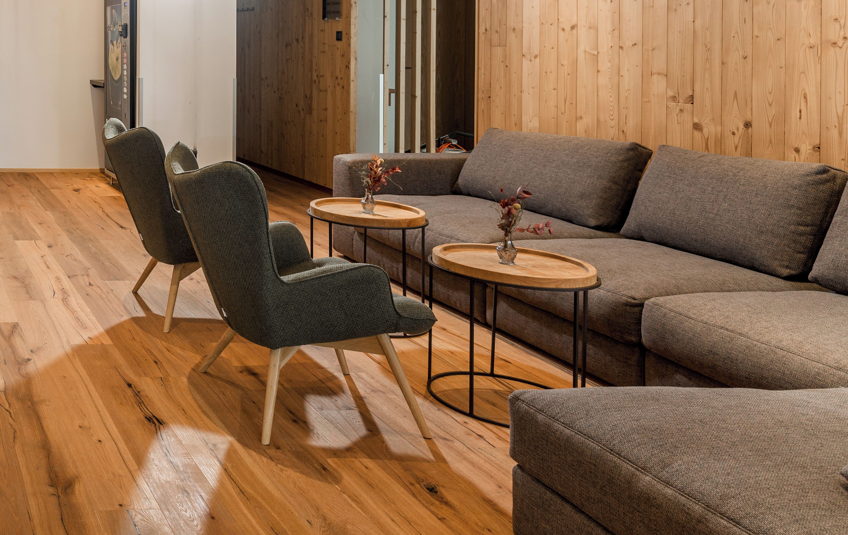 Una sala moderna con un sofá seccional, dos sillones y dos mesas redondas pequeñas con jarrones.