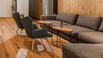 Una sala moderna con un sofá seccional, dos sillones y dos mesas redondas pequeñas con jarrones.