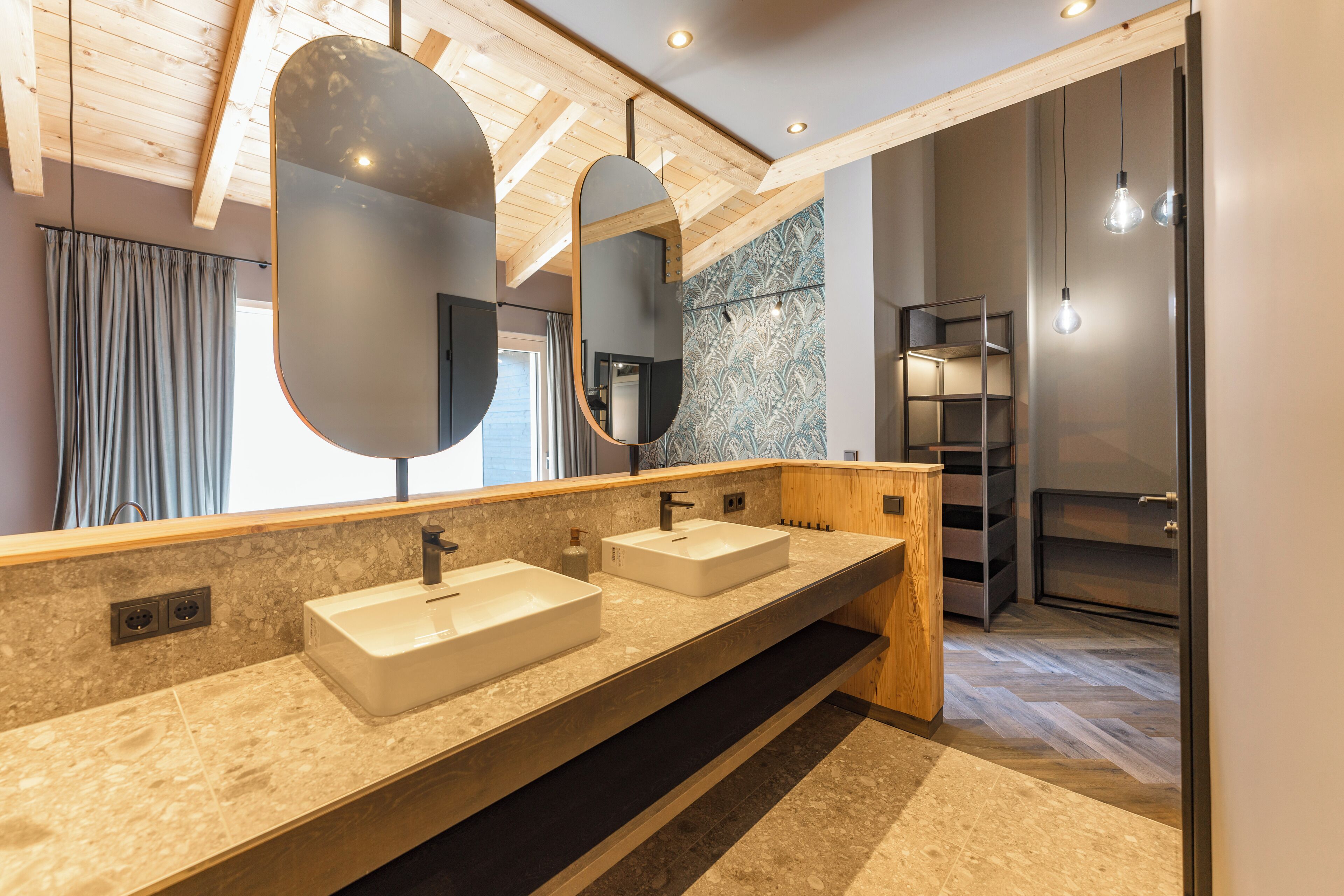 Un baño moderno con dos lavamanos, espejos grandes, vigas de techo de madera y un suelo con estampado de espiga.