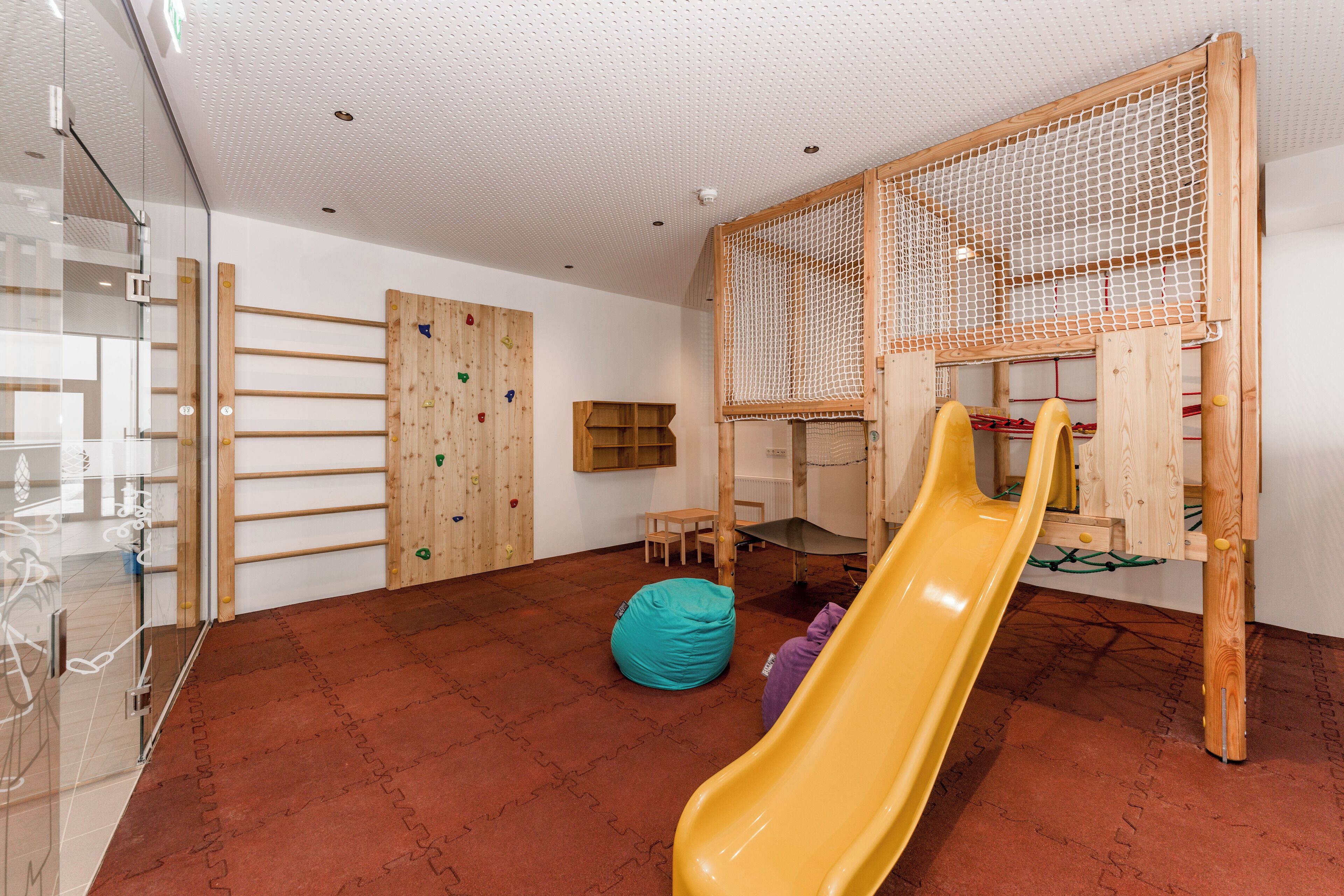 Una sala de juegos con una pared de escalada de madera, un tobogán y una estructura de red para escalar.