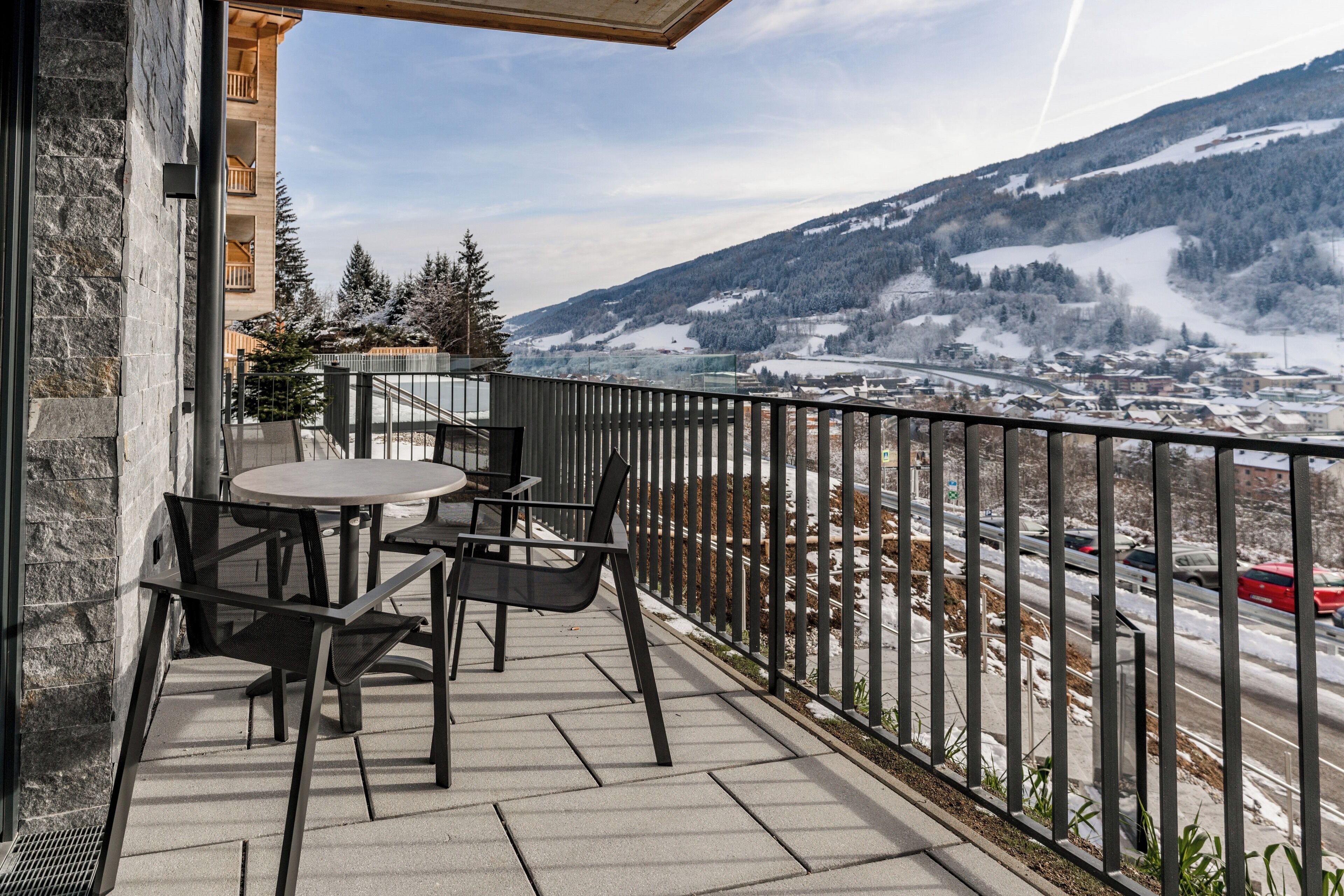 Varanda com mesa e cadeiras, com vista para uma montanha nevada e uma cidade.