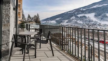 Varanda com mesa e cadeiras, com vista para uma montanha nevada e uma cidade.