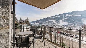 A balcony with a table and chairs, overlooking a snowy mountain and a road with cars.