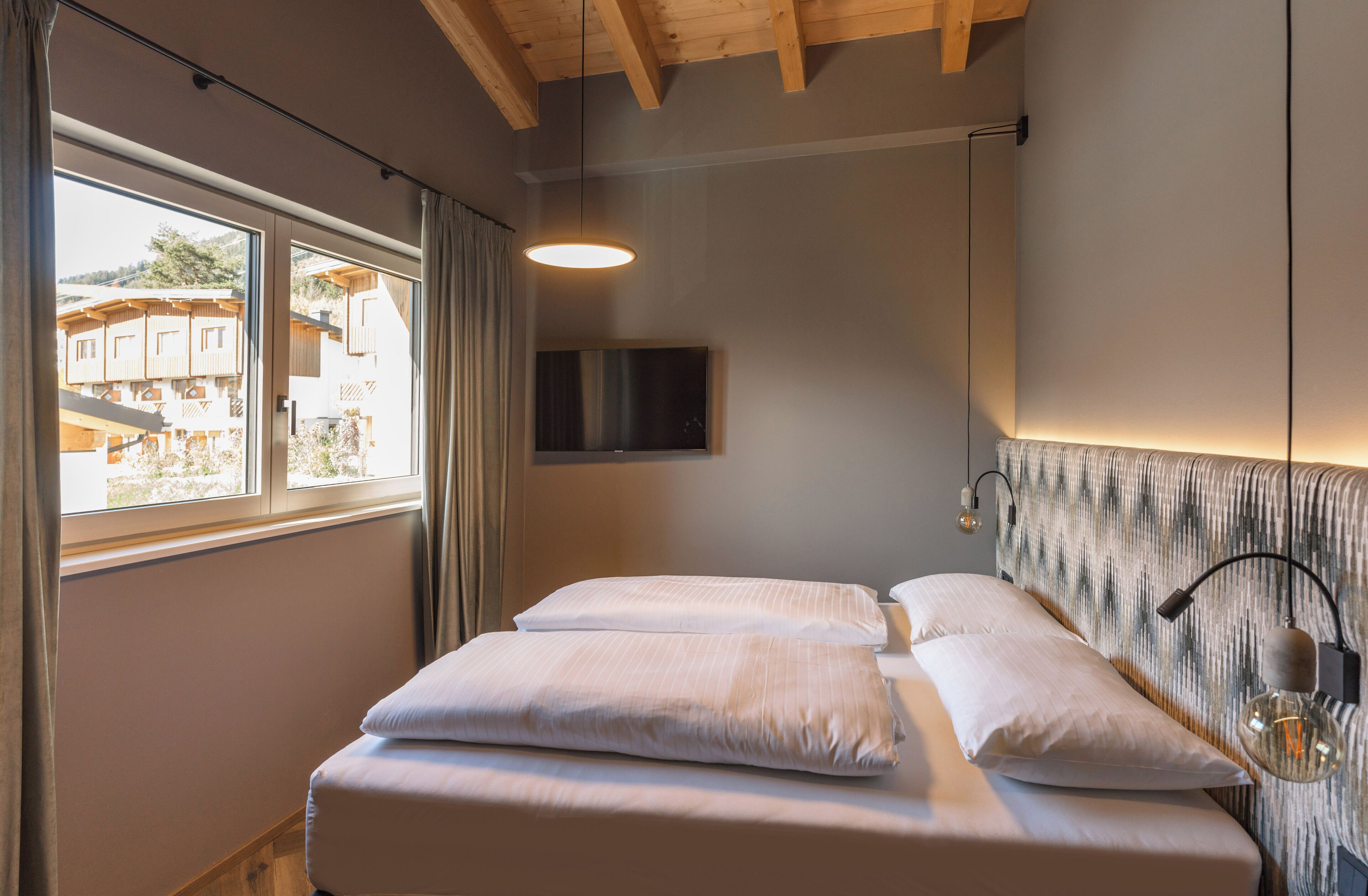 Ein Schlafzimmer mit Bett, einem an der Wand befestigten Fernseher und einem Fenster mit Vorhängen.