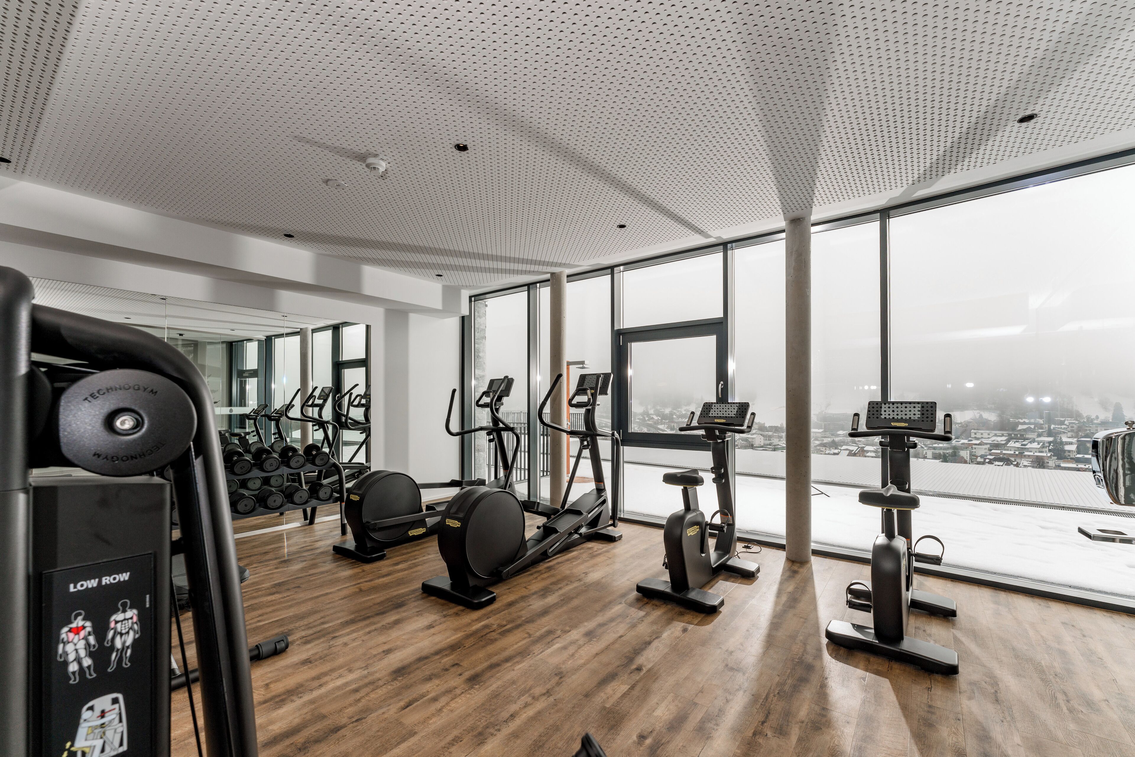 Un gimnasio moderno con máquinas de cardio, pesas y un amplio ventanal con vistas a la ciudad.
