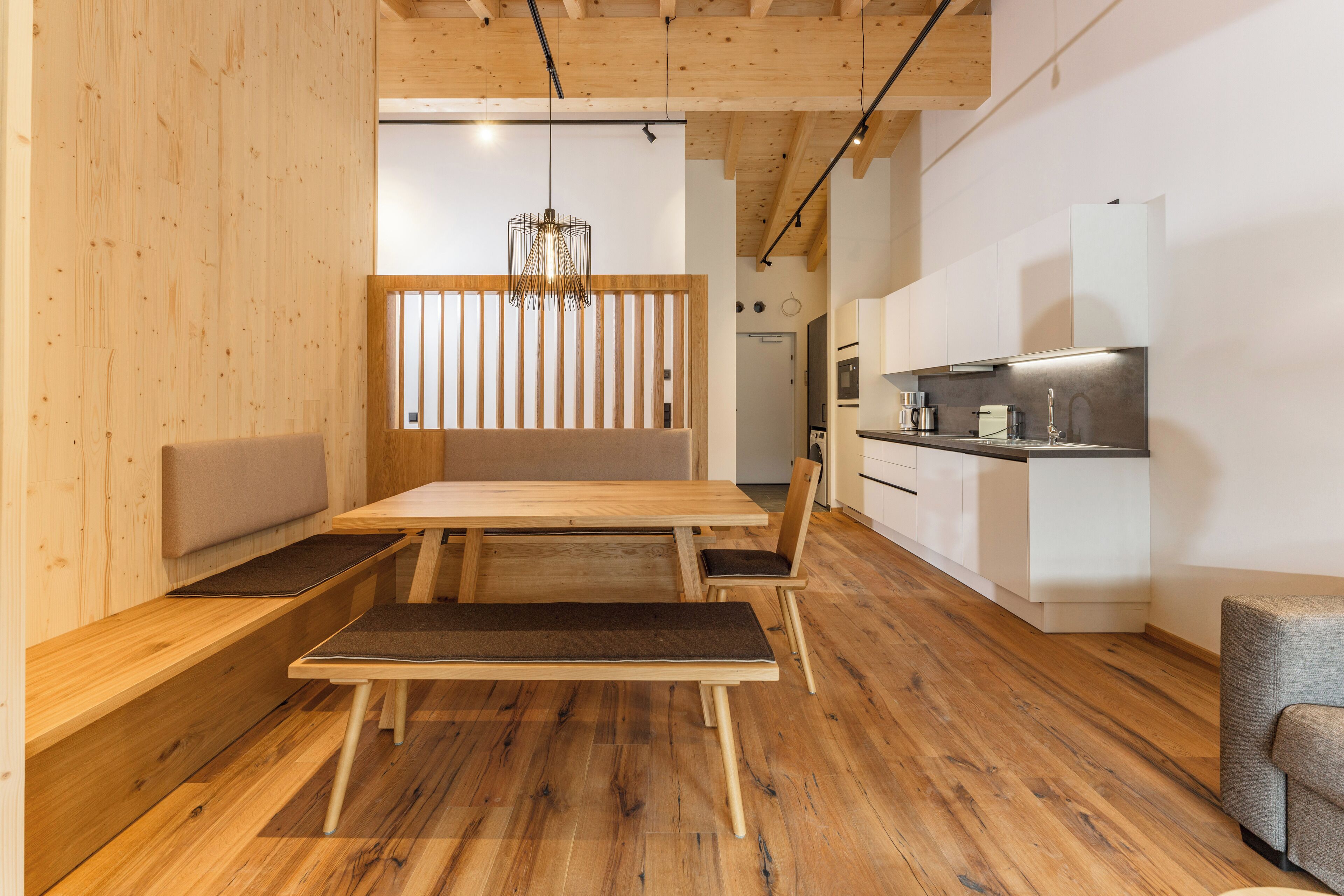 Una cocina moderna con armarios blancos y una zona de comedor de madera con un banco y sillas.