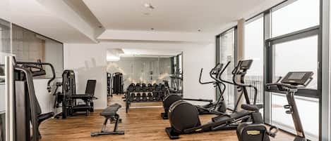 Un gimnasio moderno con máquinas de cardio, pesas libres y un espejo grande.